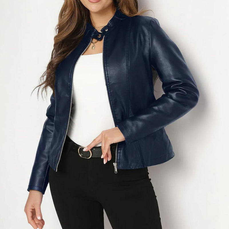 Woman wearing navy blue leather jacket, white top, black pants with belt, posing against white background