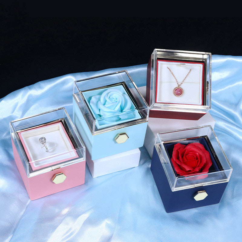 Four colorful jewelry gift boxes with clear lids, containing a ring, blue rose, pendant, and red rose on satin