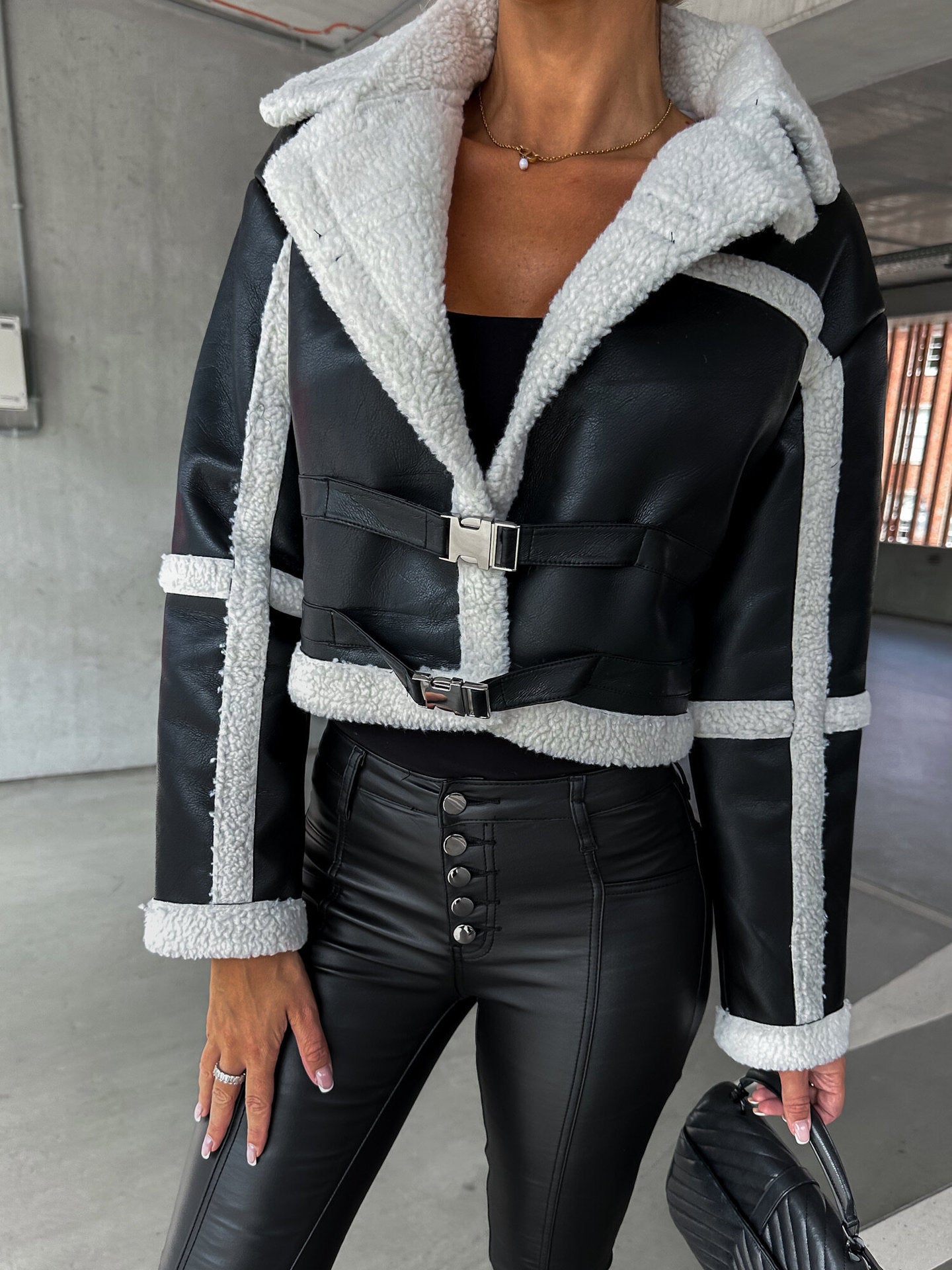 Woman wearing black faux leather cropped jacket with white sherpa lining and high-waisted black pants