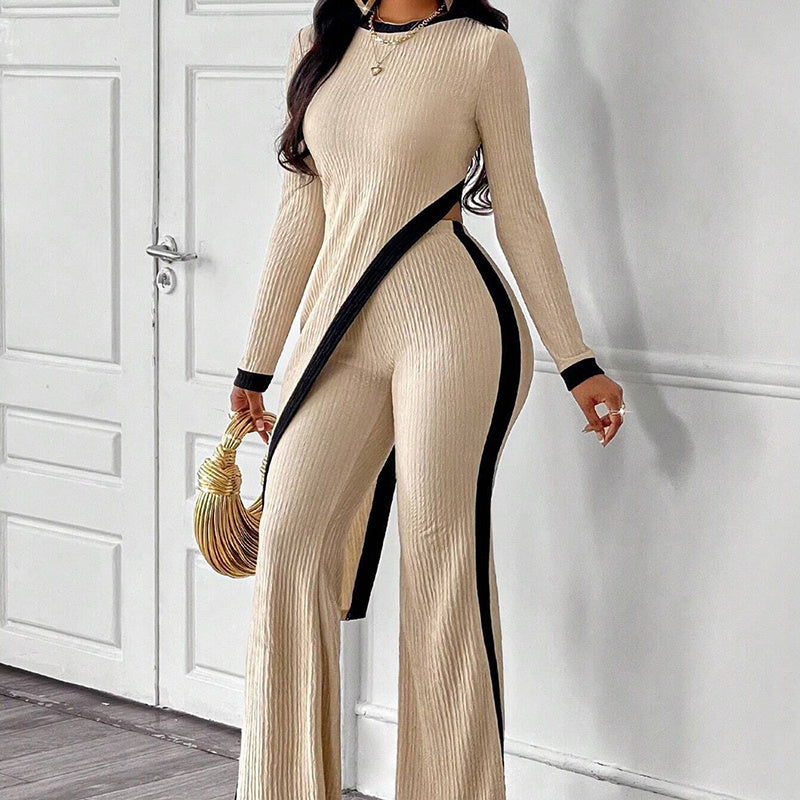 Woman wearing beige ribbed jumpsuit with black side stripes and cutout, holding gold handbag indoors