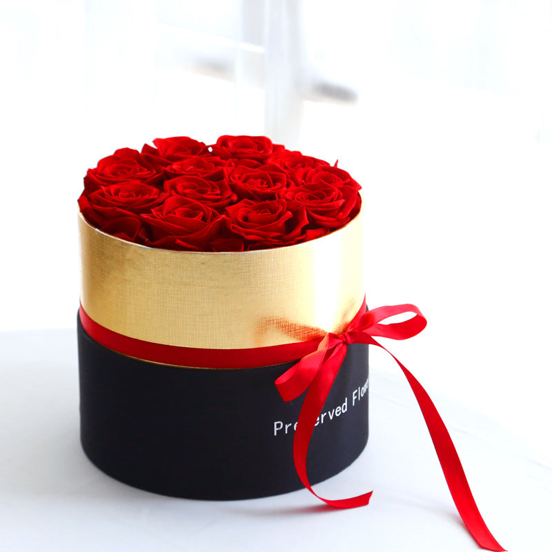 Round black and gold gift box with a red ribbon, filled with vibrant red preserved roses