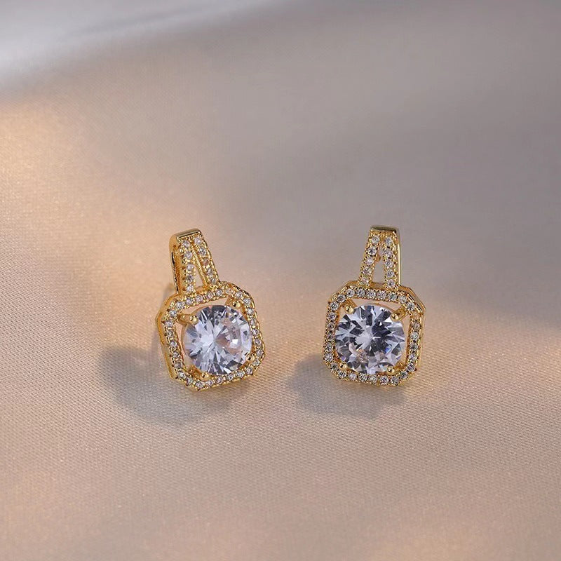 Pair of gold earrings with large clear gemstones surrounded by small crystals on beige fabric