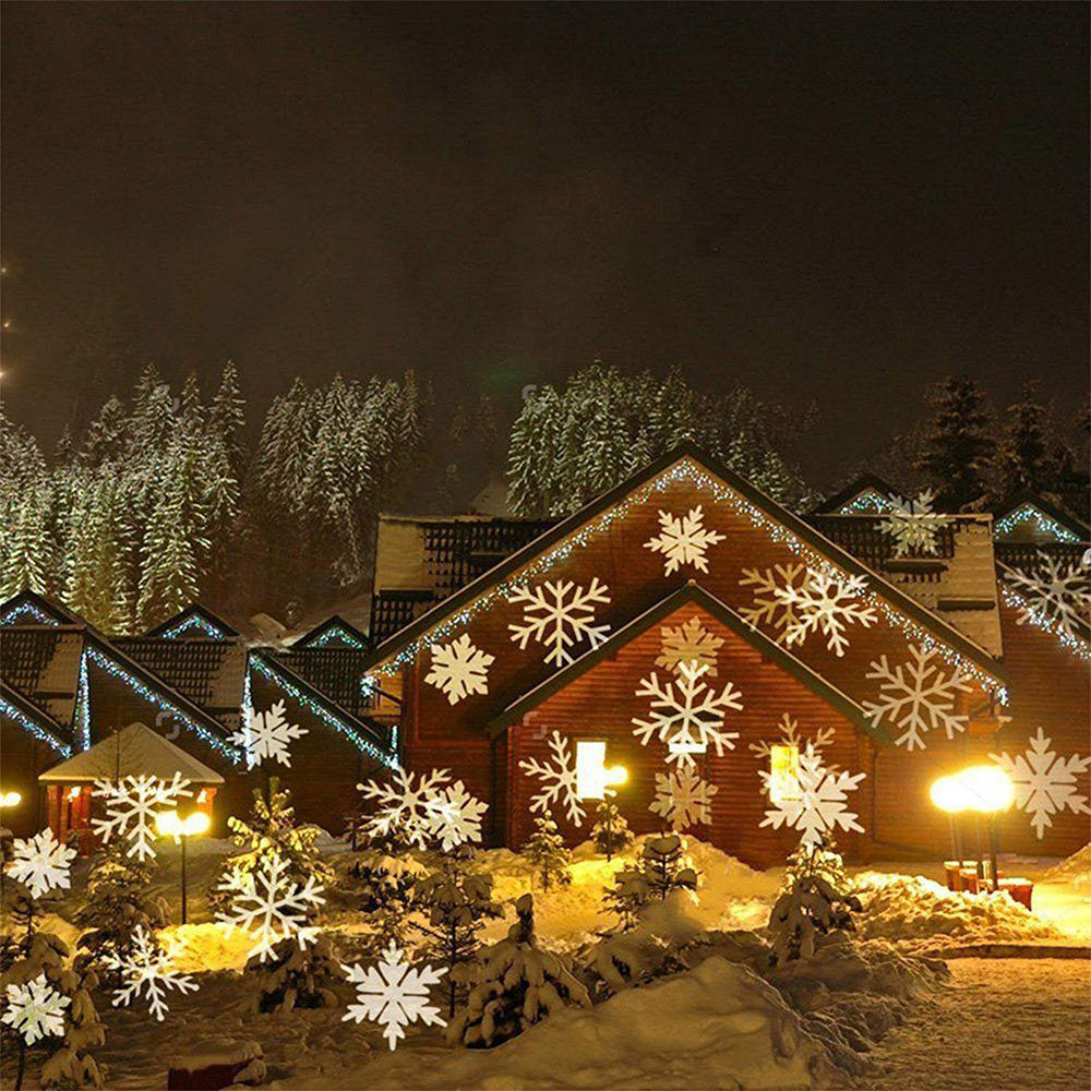 Snow-covered cabins decorated with glowing lights and large snowflake projections in a winter forest at night
