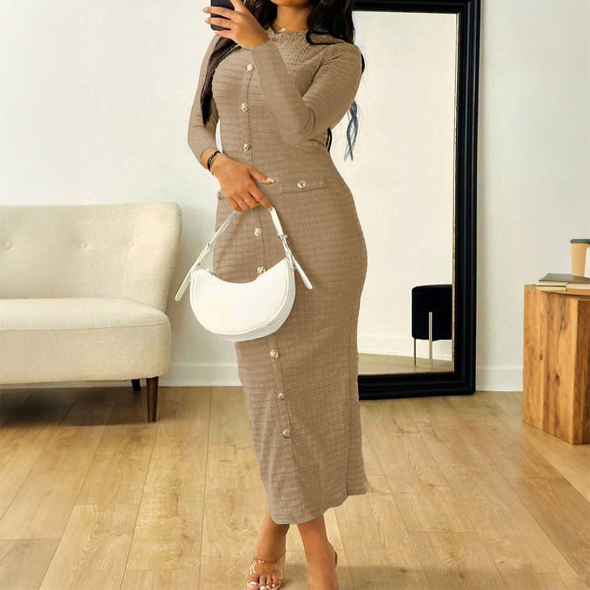 Woman in beige buttoned midi dress holding white handbag in modern room with mirror and sofa