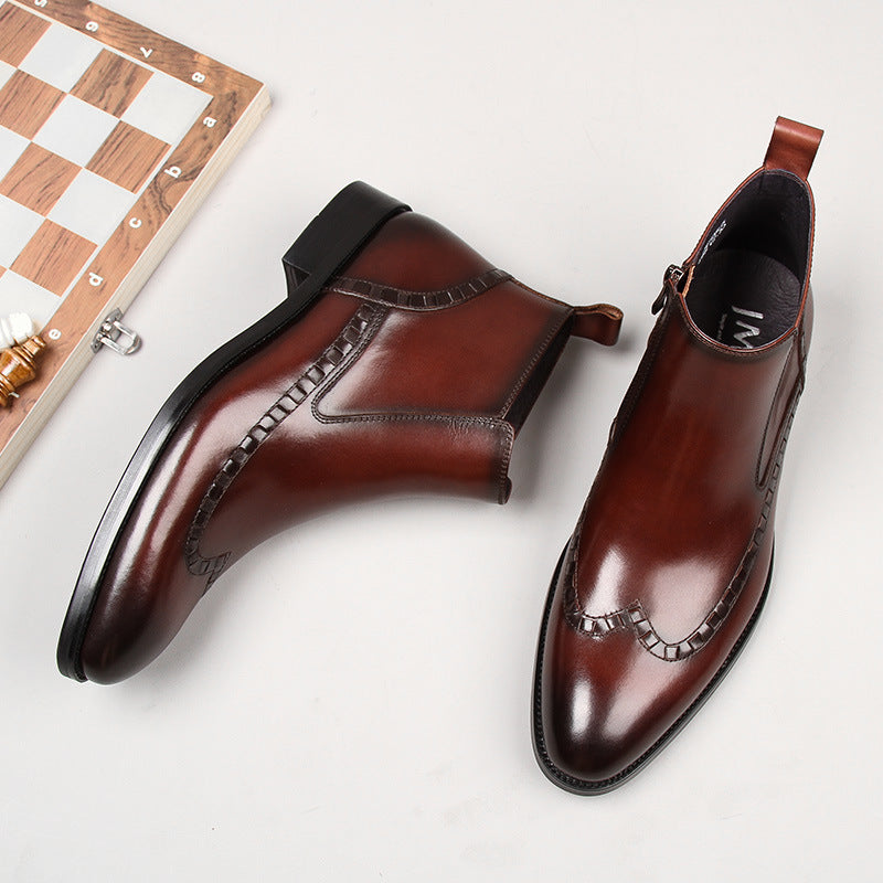 Pair of polished brown leather ankle boots with decorative stitching on white background, next to a wooden chessboard