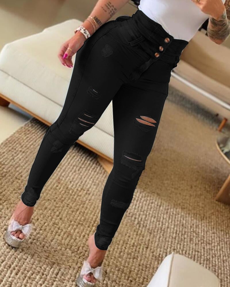 Woman wearing high-waisted black ripped skinny jeans and white top indoors on carpeted floor