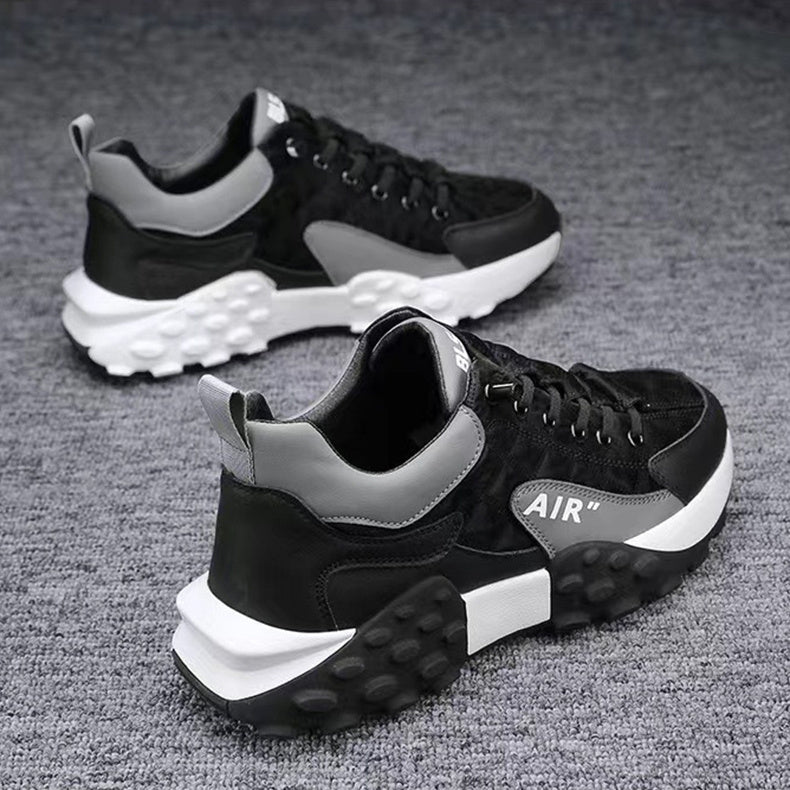 Black and gray athletic sneakers with chunky white and black textured soles on gray carpet