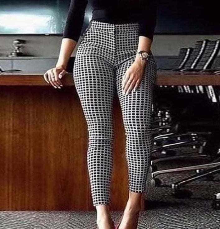 Woman wearing black and white checkered skinny pants standing in office with chairs and wooden table