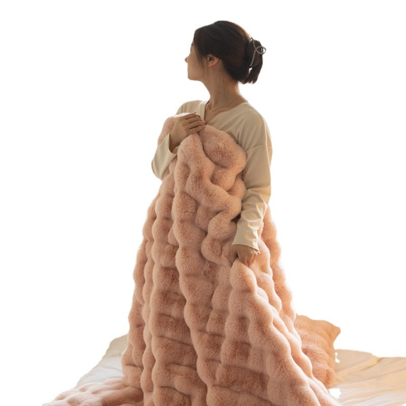 woman wrapped in soft pink plush fur blanket with wavy texture sitting on white surface