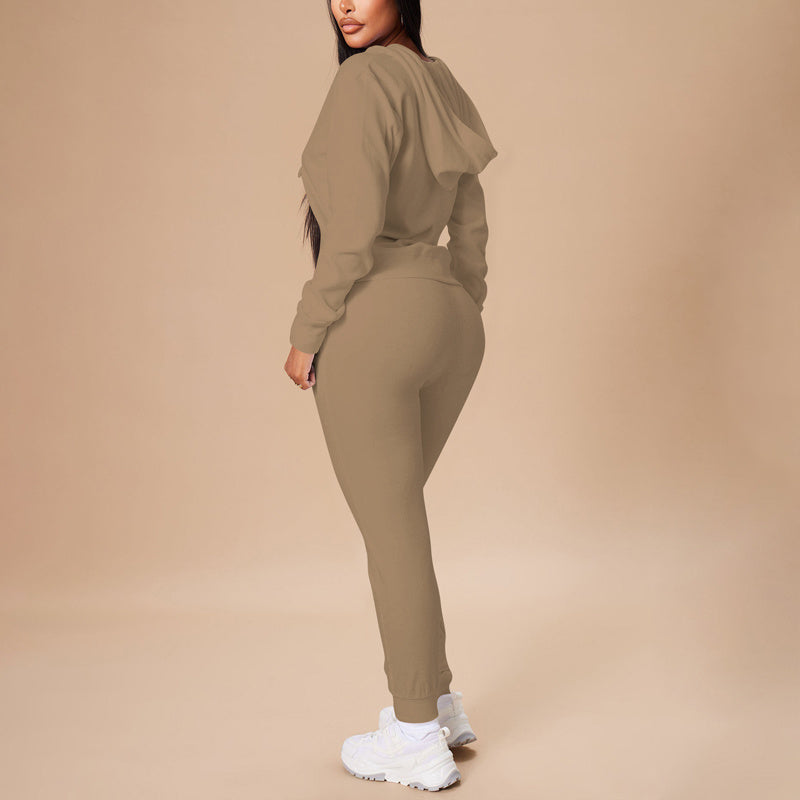 Woman wearing beige hooded sweatshirt and matching joggers with white sneakers on neutral background