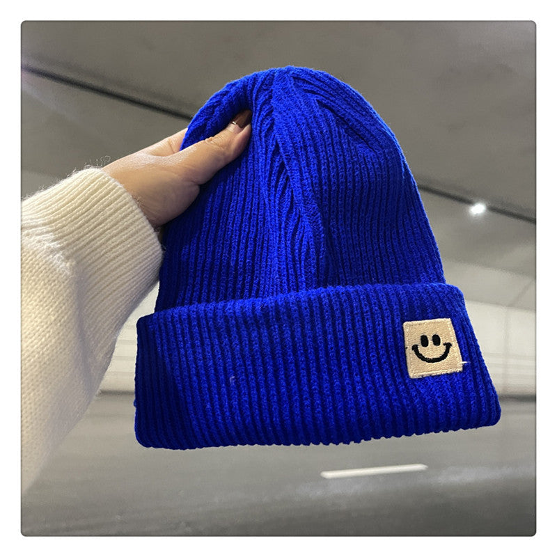 Hand holding vibrant blue ribbed knit beanie with folded cuff and smiley face patch