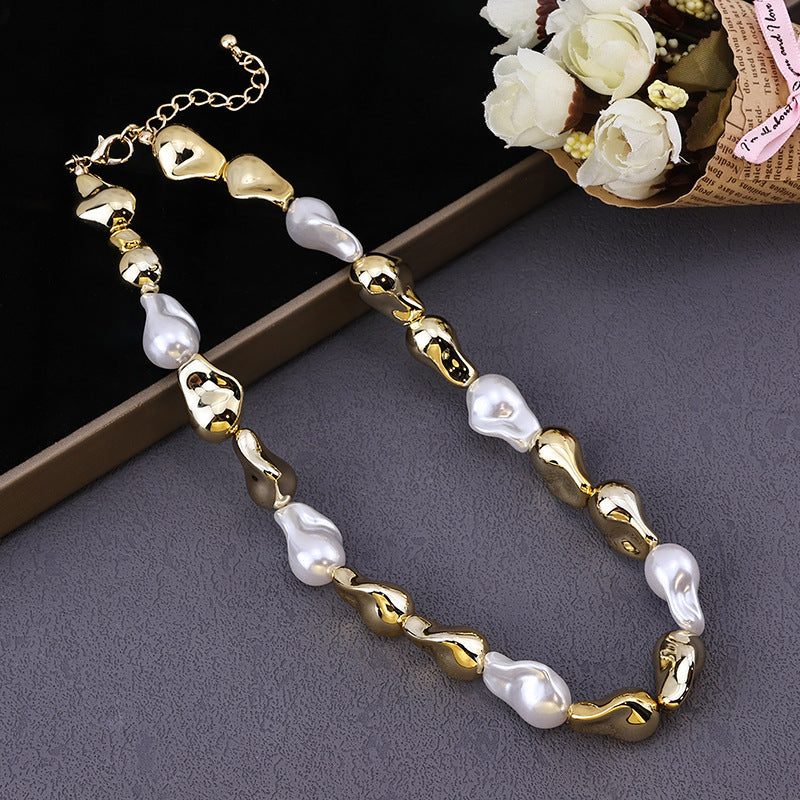 Gold and white irregular pearl necklace displayed on gray surface with white flower bouquet