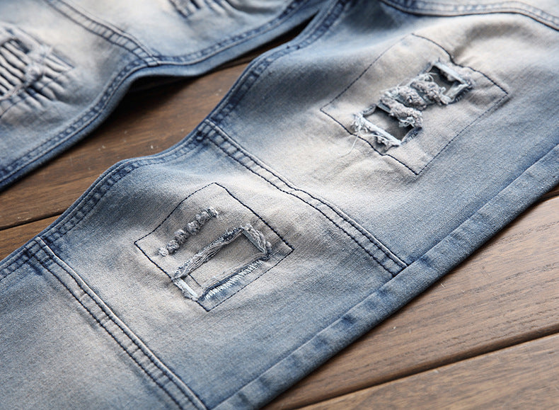 Close-up of light blue distressed denim jeans with stitched rectangular patches on wooden surface