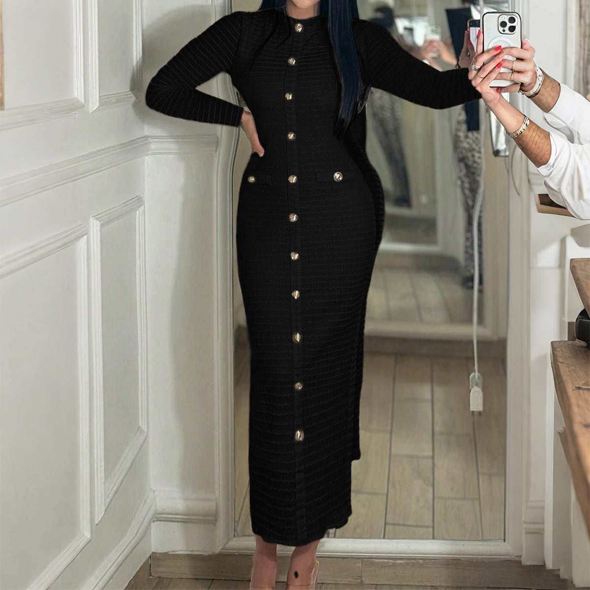 Woman wearing long black buttoned knit dress with gold buttons, taking mirror selfie indoors