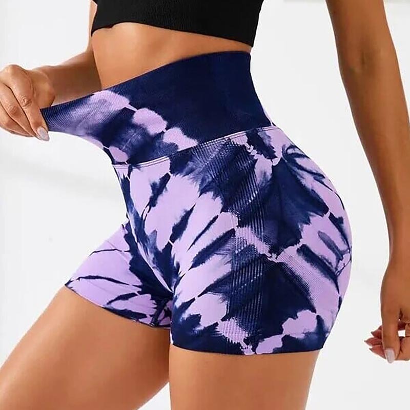 Woman wearing high-waisted tie-dye purple and navy blue workout shorts stretching the waistband