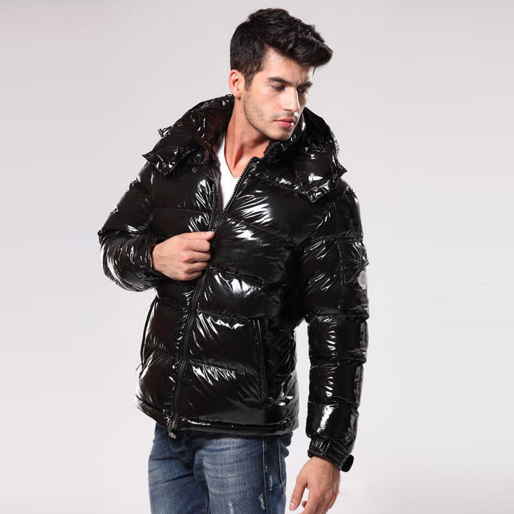 Man wearing shiny black puffer jacket with hood and blue jeans against plain background