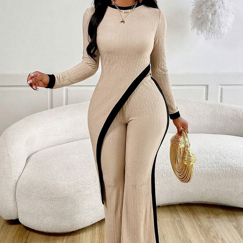 Woman wearing beige ribbed jumpsuit with black diagonal trim, holding gold textured handbag in modern living room