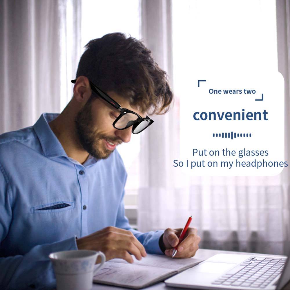 Man wearing black smart glasses with built-in headphones, working at desk with laptop and notebook