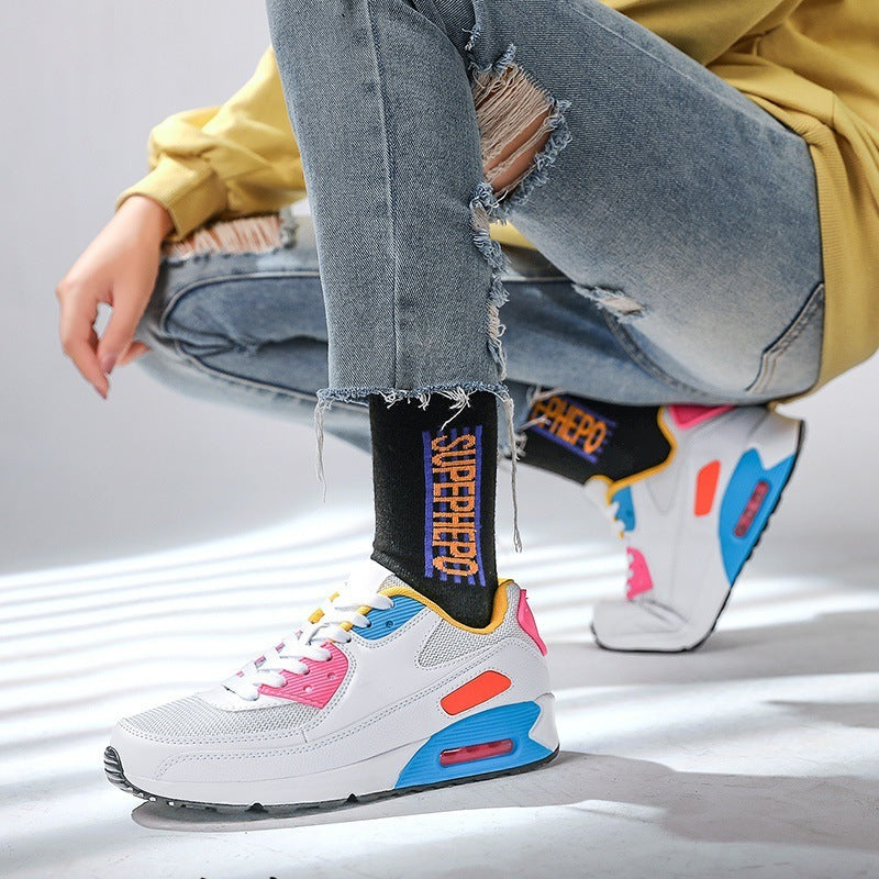 Person wearing ripped blue jeans, black 'SUPERHERO' socks, and white colorful sneakers with pink and blue accents