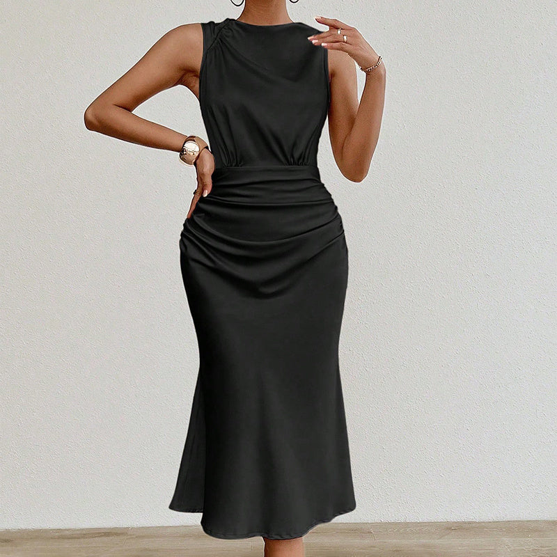 Woman wearing sleeveless black midi dress with ruched waist standing against white wall
