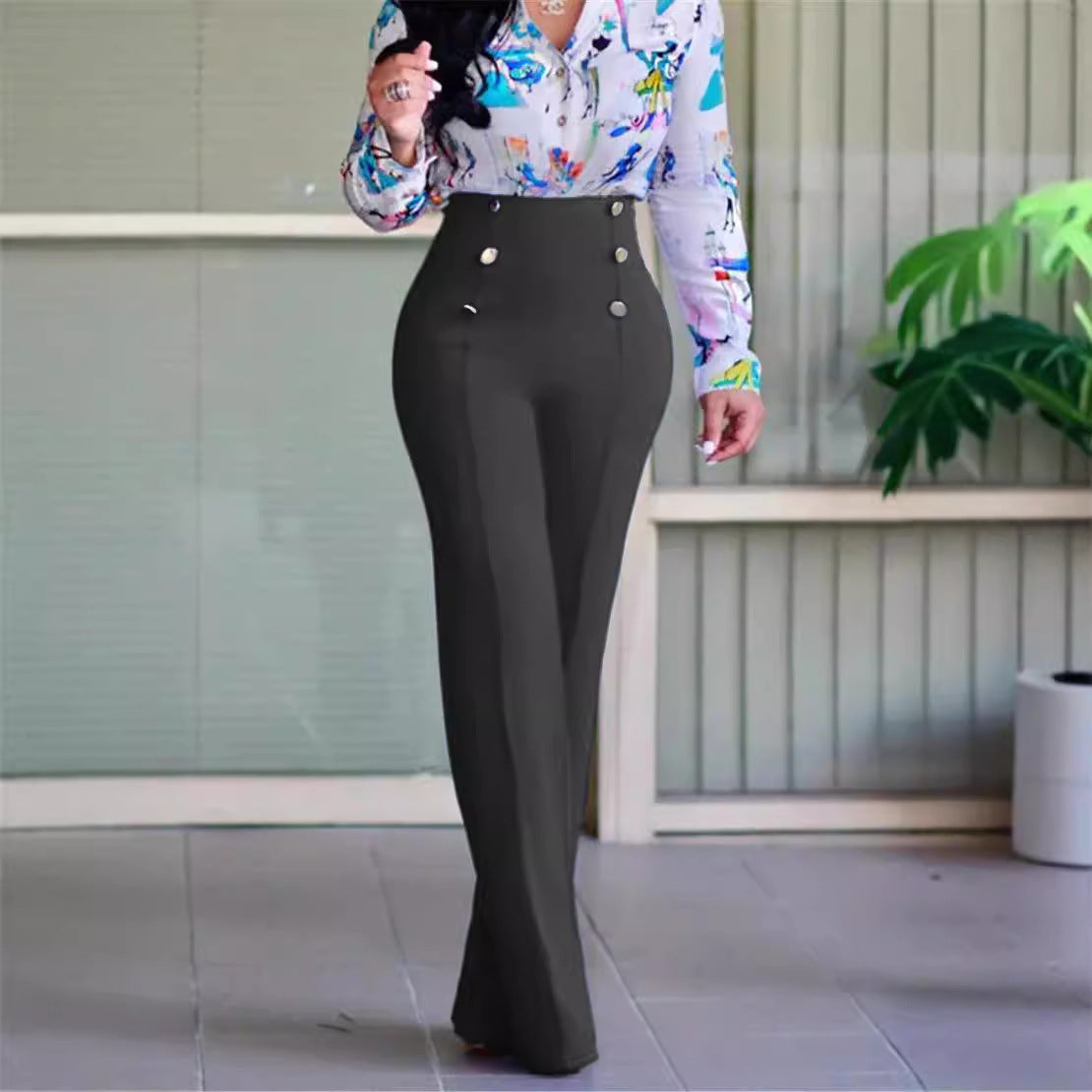 Woman wearing high-waisted black wide-leg pants with gold buttons and floral blouse walking indoors