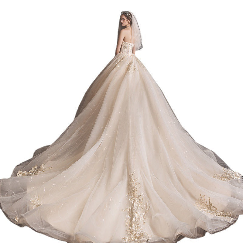 Elegant bride in strapless ivory wedding gown with long, flowing tulle train and gold embroidery