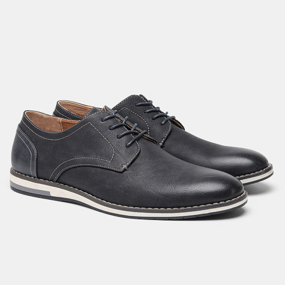 Pair of black leather casual men's lace-up shoes with white and black sole on gray background