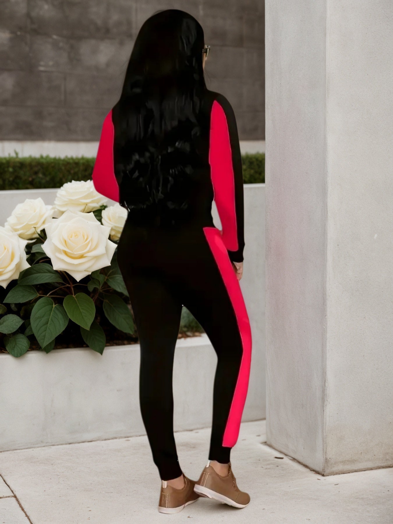 Woman wearing a black and red athletic tracksuit with sneakers standing near white roses outdoors