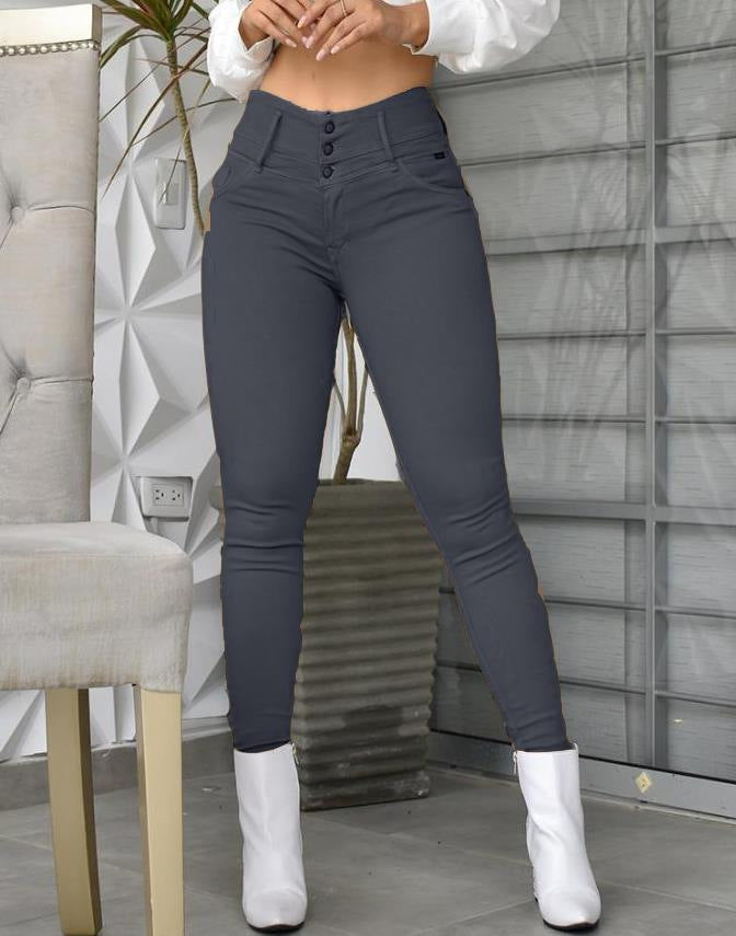 Woman wearing high-waisted dark gray skinny pants and white ankle boots, indoor setting