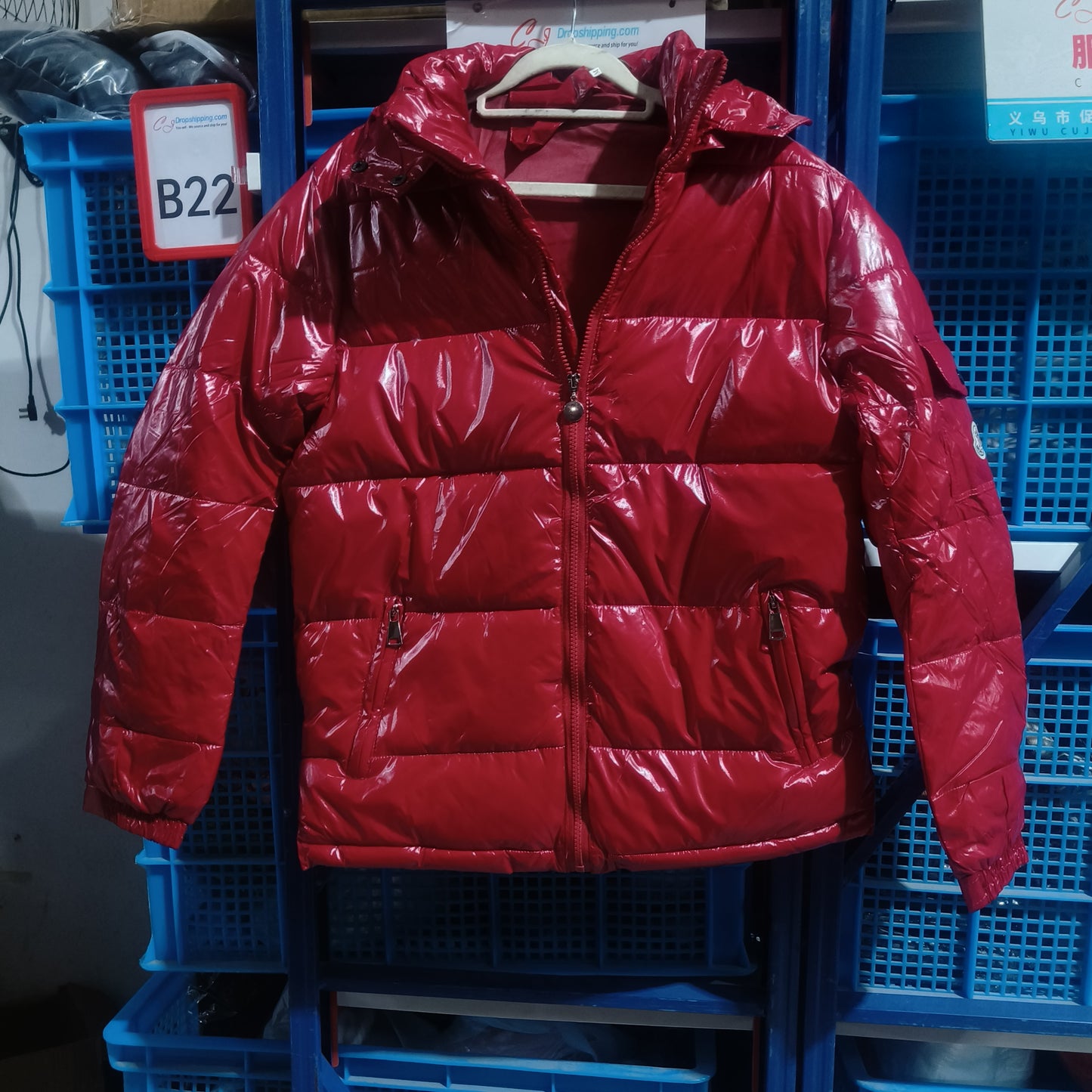 Shiny red puffer jacket with zipper and pockets hanging on a wooden hanger in storage area