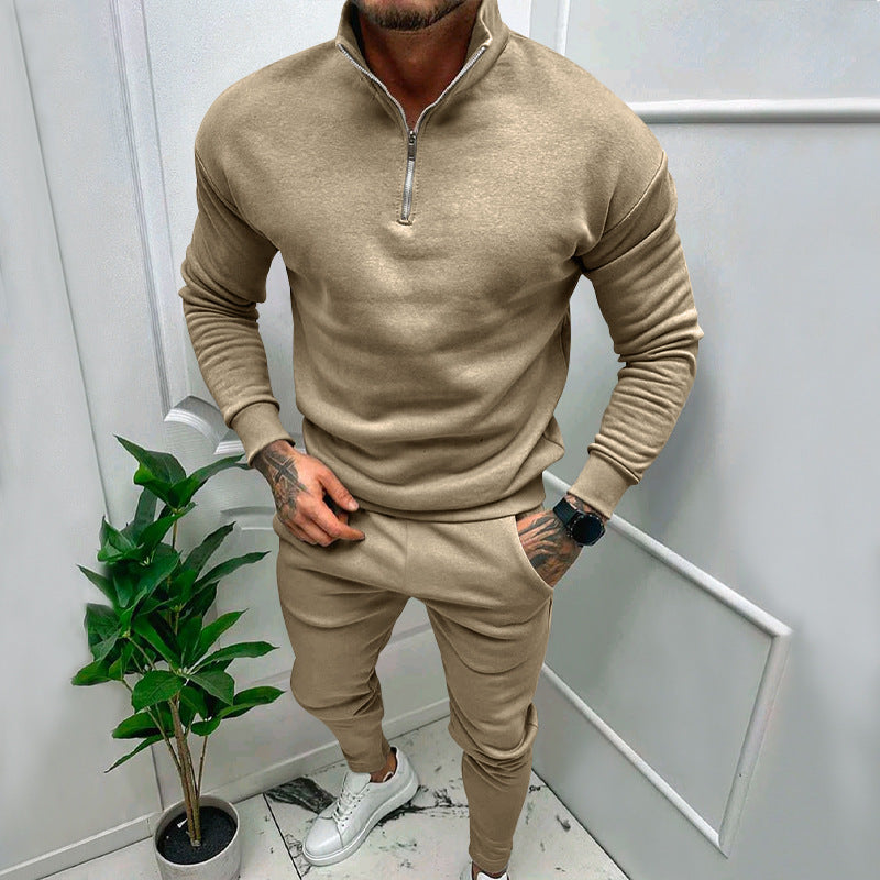 Man wearing beige quarter-zip sweatshirt and matching joggers with white sneakers, standing indoors near potted plant