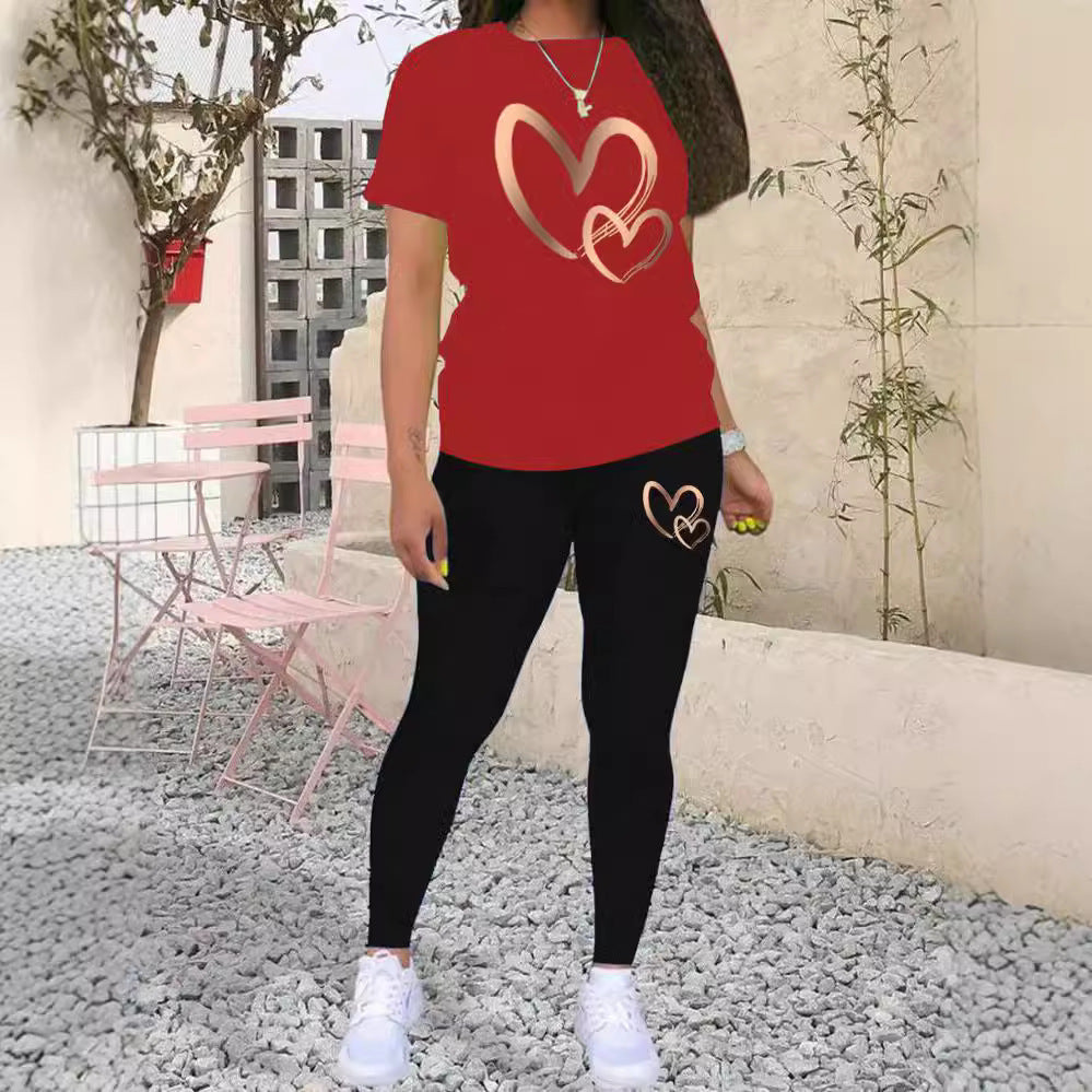 Woman wearing red t-shirt and black leggings with heart designs, standing on gravel patio with pink chairs