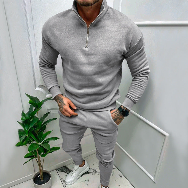 Man wearing gray zip-up sweatshirt and matching joggers with white sneakers in modern indoor setting