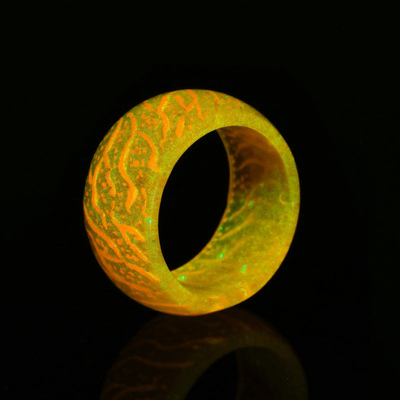 Glowing orange and green resin ring with intricate patterns against black background