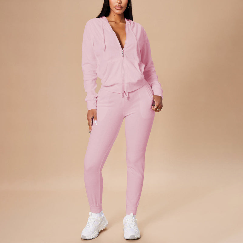 Woman wearing pink zip-up hoodie and matching jogger pants with white sneakers on beige background