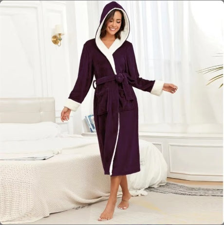 Woman wearing cozy purple hooded bathrobe with white trim in a bright bedroom setting