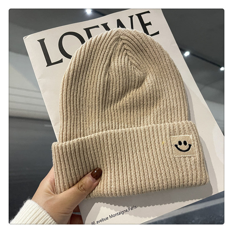 Beige ribbed knit beanie with smiley face patch held over a LOEWE magazine