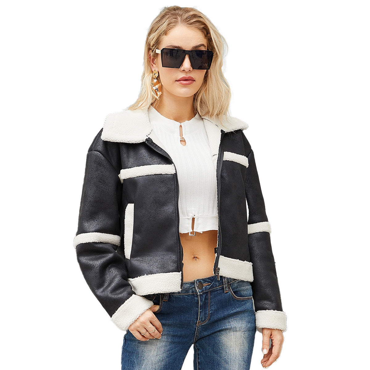 Woman wearing black and white faux shearling jacket, white crop top, blue jeans, and oversized sunglasses