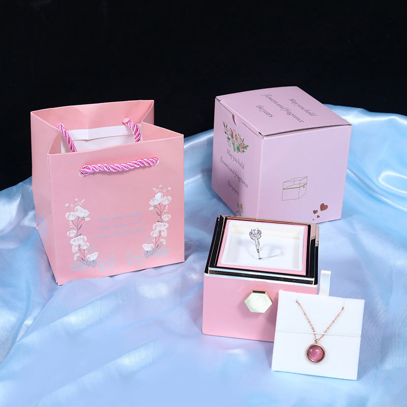Pink gift bag, jewelry box with diamond ring, and pink pendant necklace on blue satin