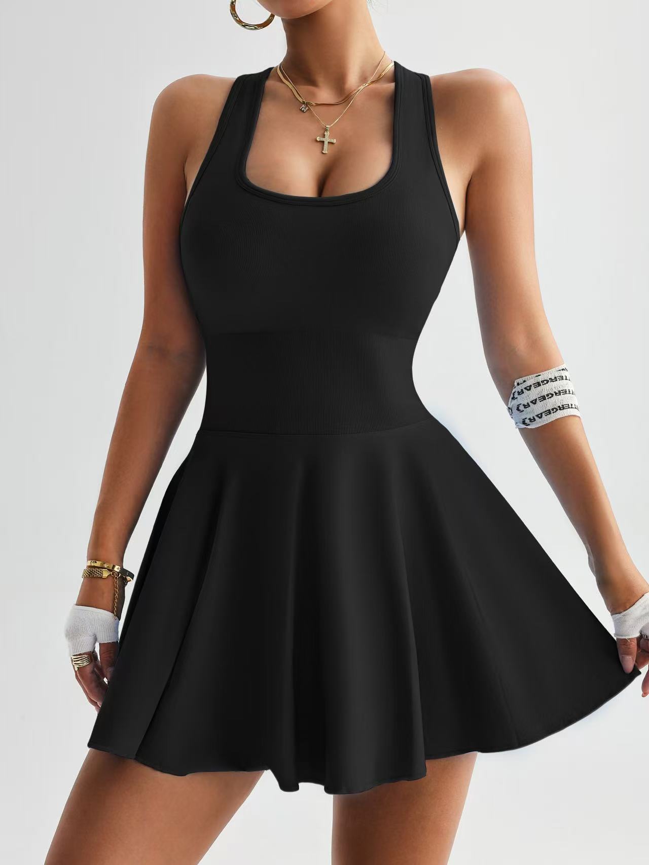 Woman wearing a black sleeveless fit-and-flare dress with gold necklaces and hoop earrings