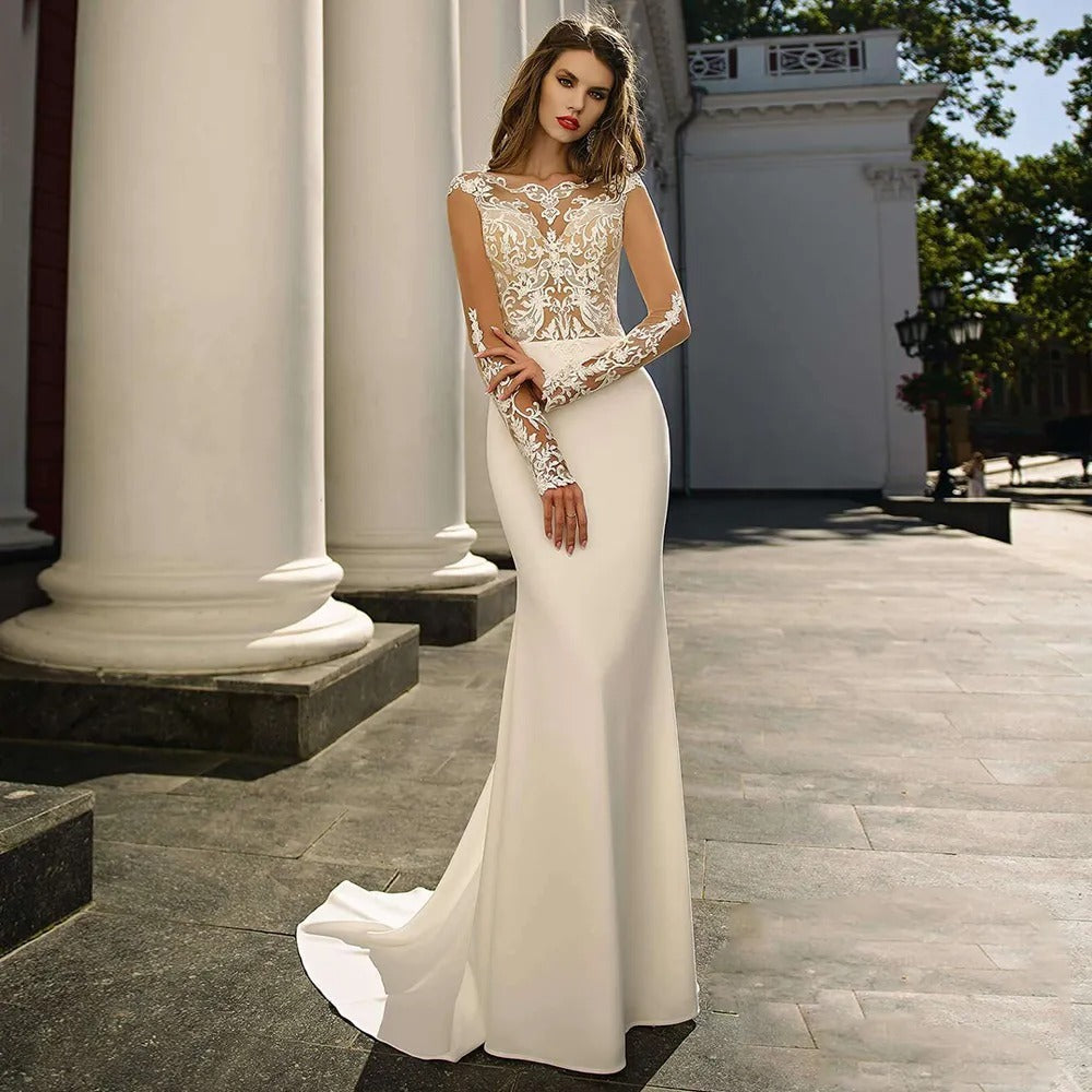 Elegant woman in a white bridal gown with lace bodice and long sleeves standing outdoors by classical columns