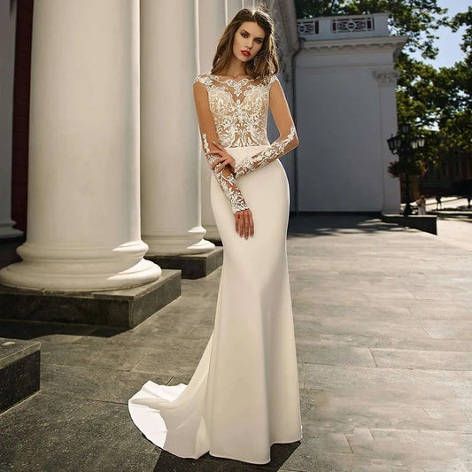 Elegant woman in a white bridal gown with lace bodice and long sleeves standing outdoors by classical columns