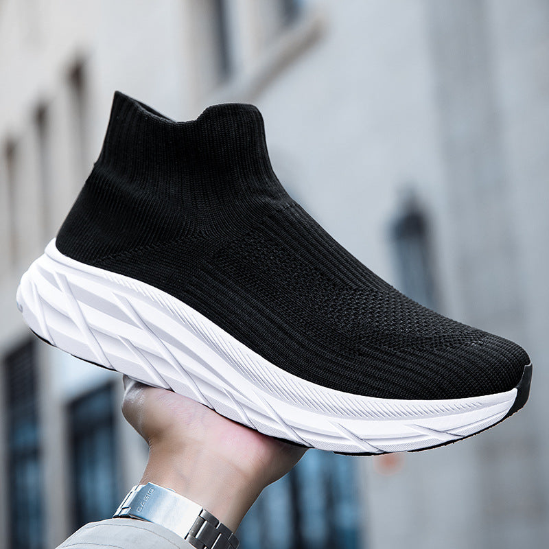 Black sock-style knit sneaker with thick white textured sole held outdoors
