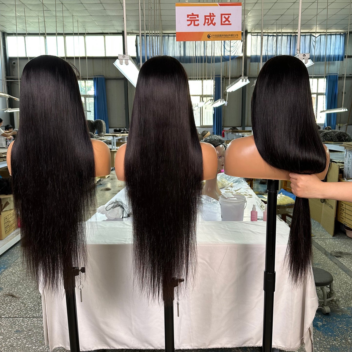 Three mannequin heads with long, straight black hair displayed in a bright hair factory showroom