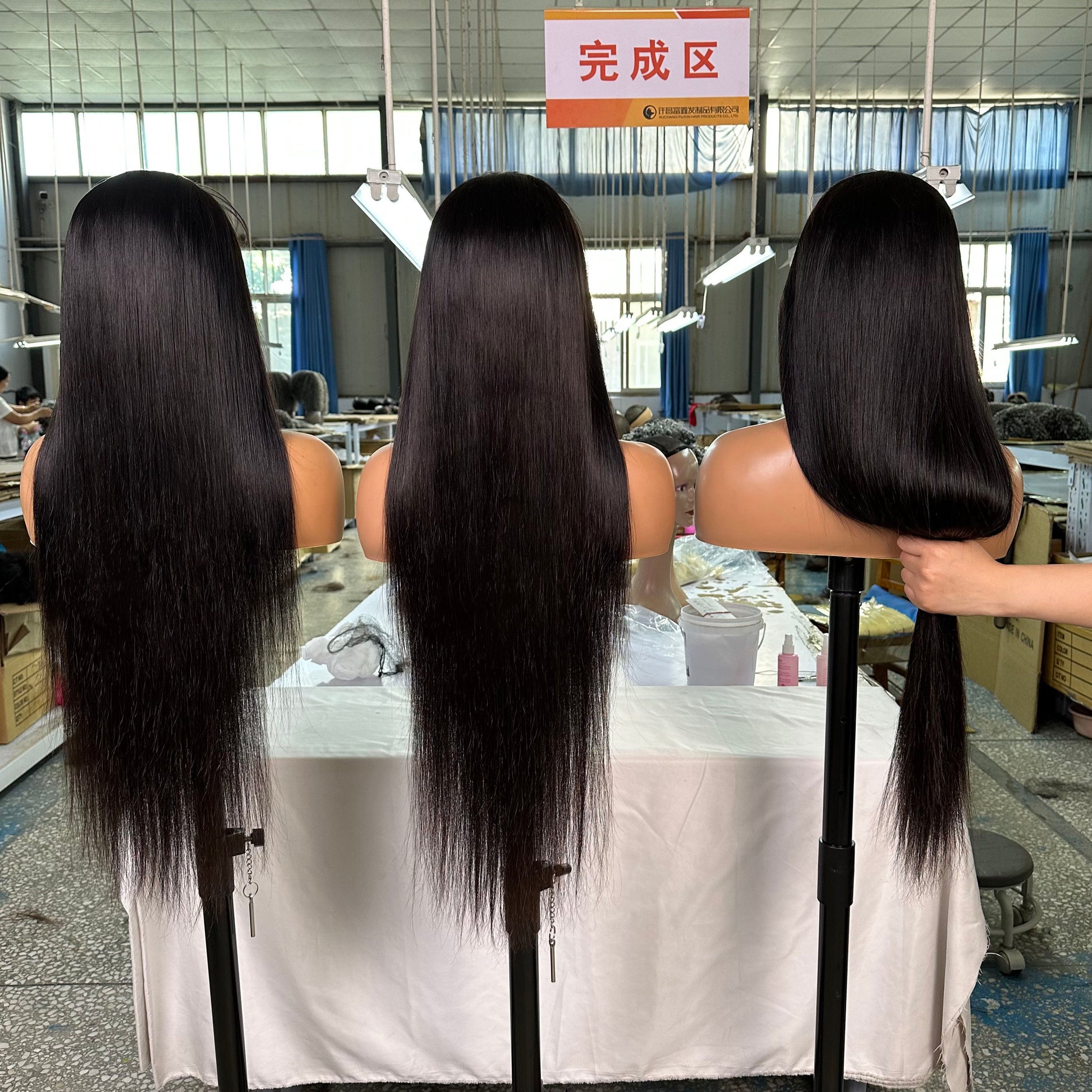Three mannequin heads with long, straight black hair displayed in a bright hair factory showroom