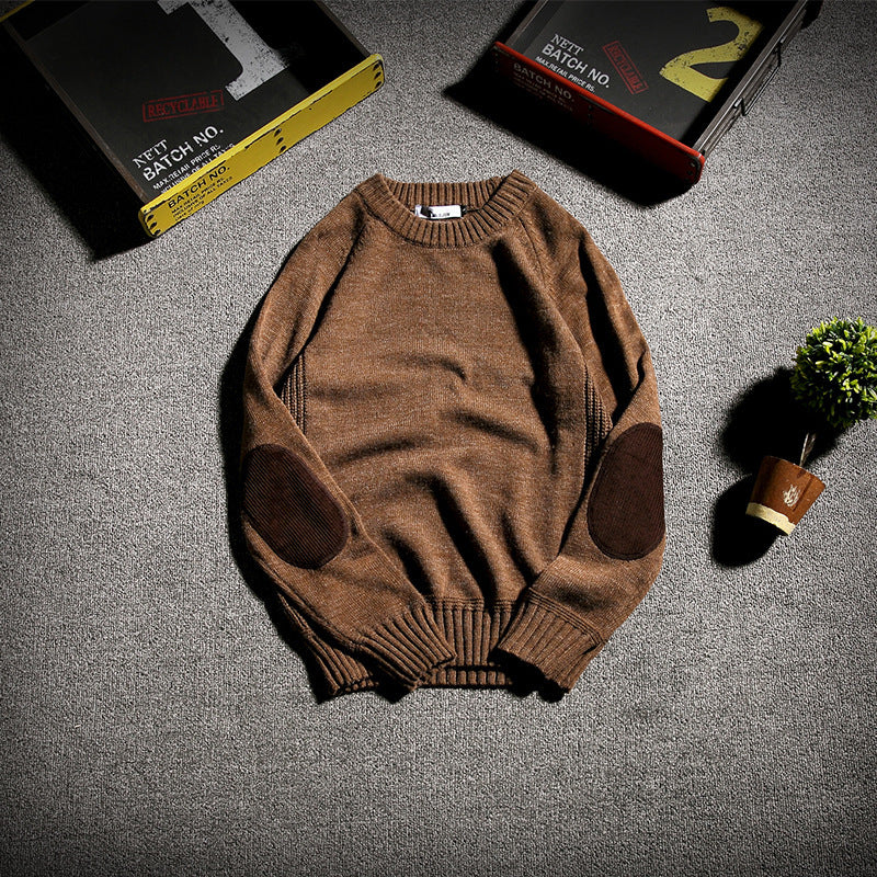 Brown knit sweater with dark elbow patches on gray carpet, surrounded by vintage storage boxes and small potted plant