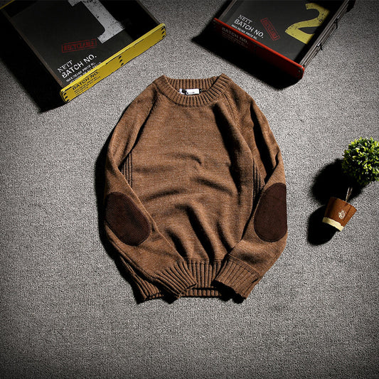 Brown knit sweater with dark elbow patches on gray carpet, surrounded by vintage storage boxes and small potted plant