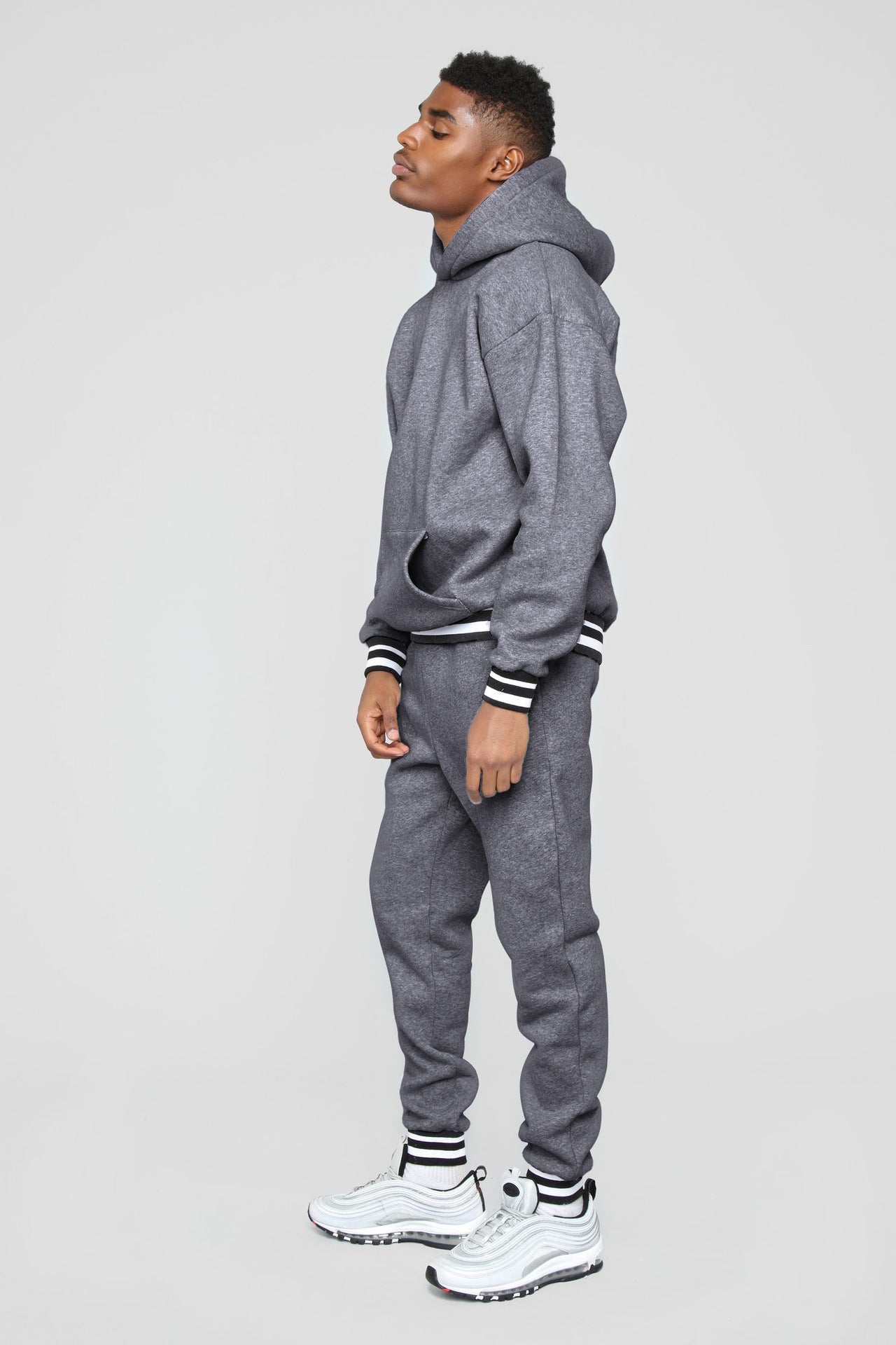 Man wearing grey hoodie with black and white striped cuffs and matching sweatpants with white sneakers