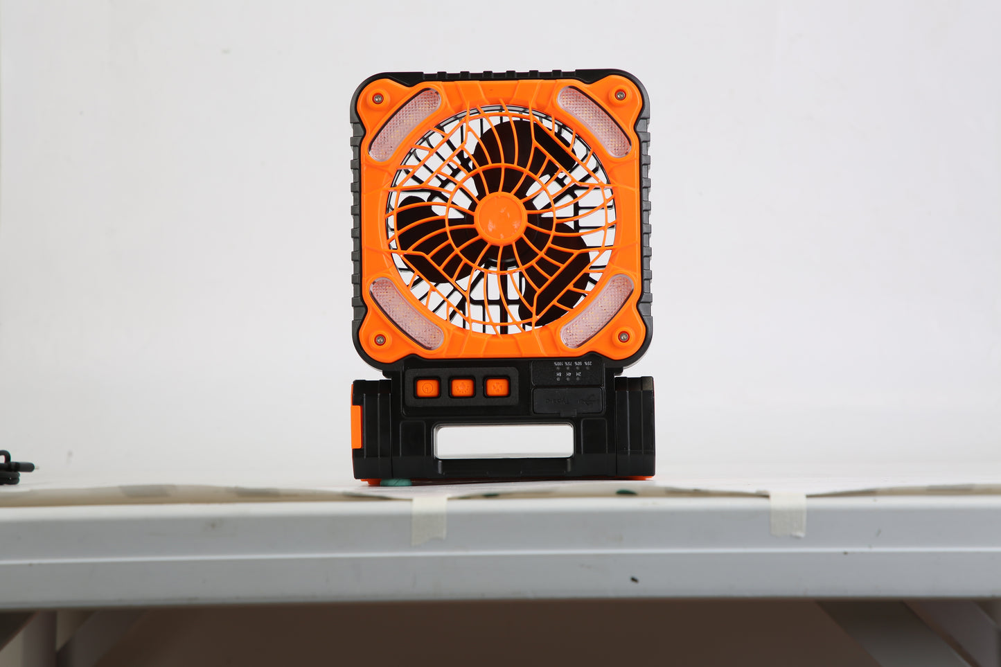 Orange and black portable fan with buttons on white table against plain wall