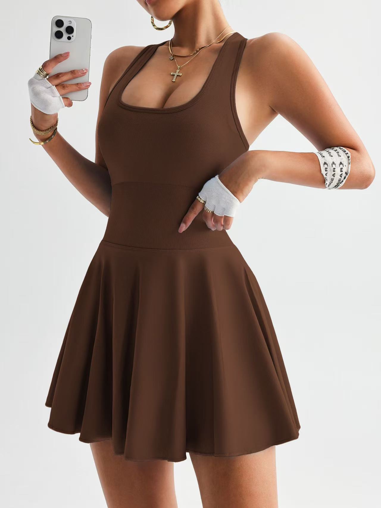 Woman wearing brown sleeveless skater dress taking selfie with smartphone on white background